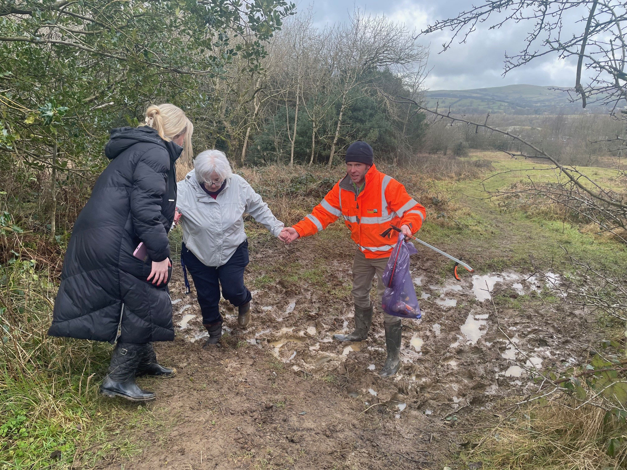 A photograph showing three people walking through mud on Gib Hill.